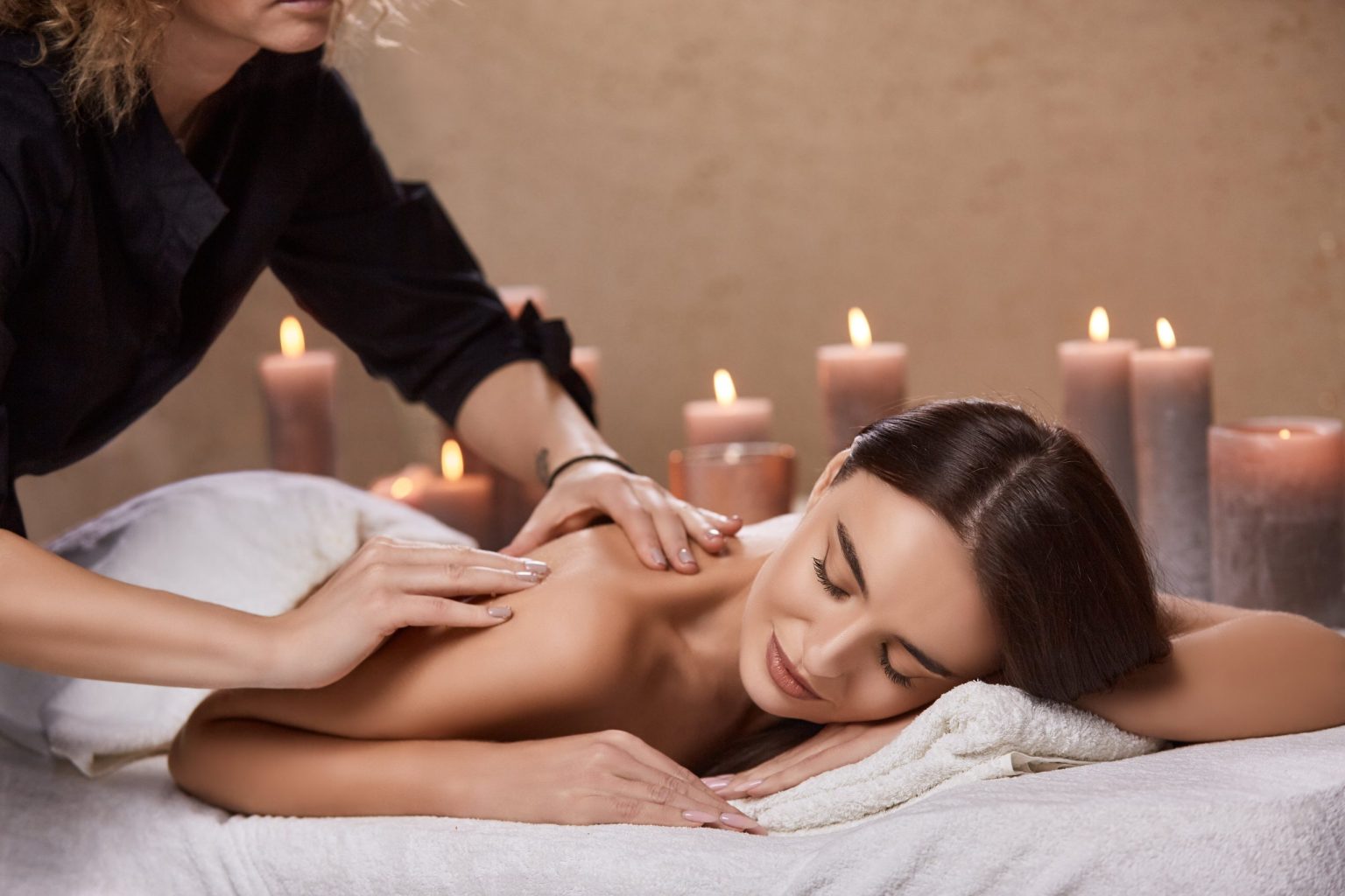 A professional therapist massaging a draped client's upper back in a candlelit spa room